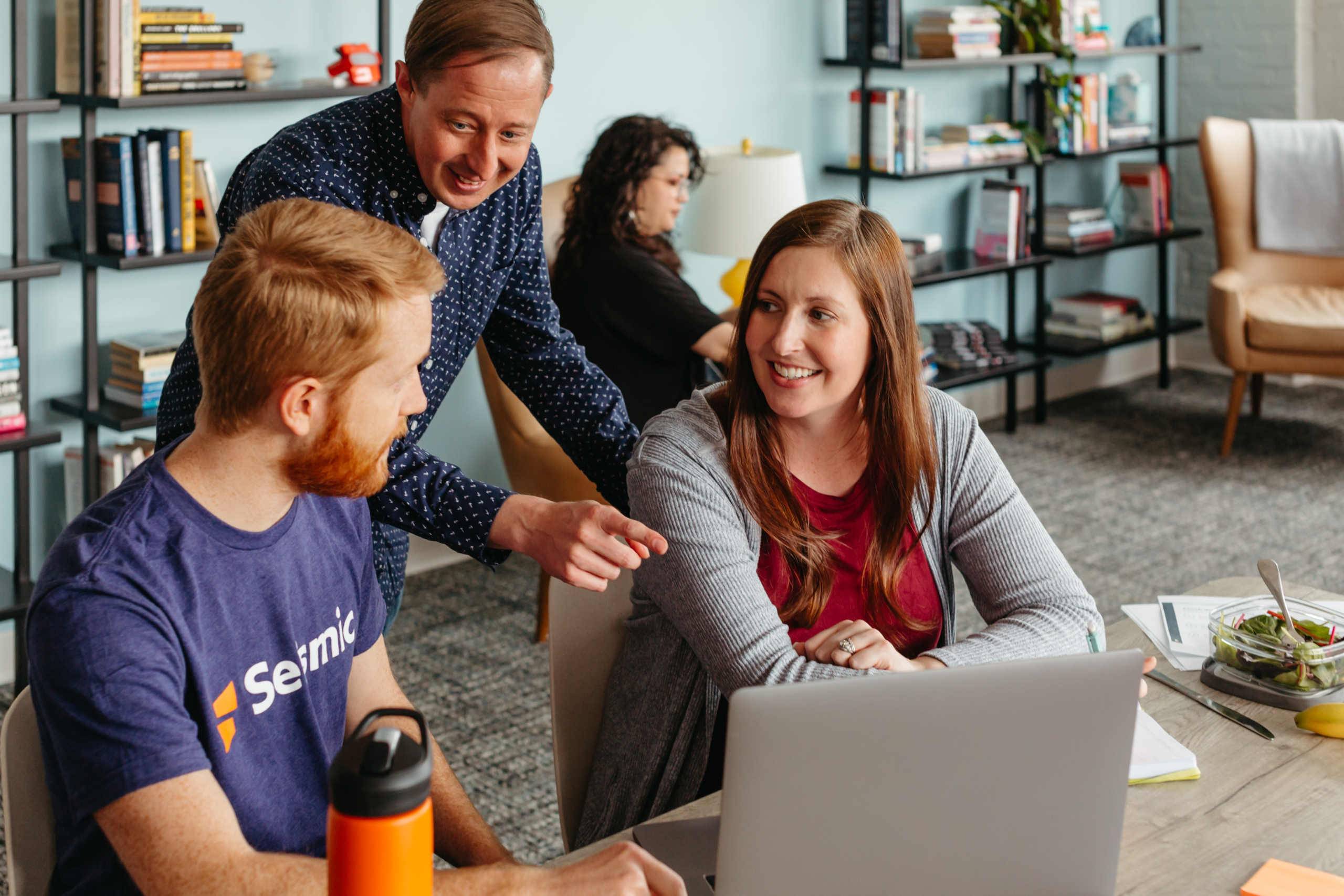 A small group of coworkers gathered around a laptop.
